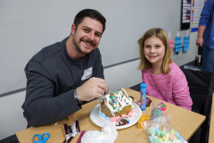 A man and a young girl are decorating gingerbread houses together.