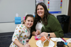 Woman and child at a table with gingerbread house in front of them.