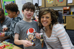 Woman in striped shirt posing with young boy holding a gingerbread man at a table.