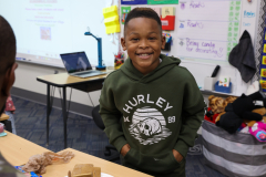 Boy in green hoodie posing for picture in classroom.