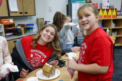 Two people standing at a table decorated for Christmas, with gingerbread houses in front of them.