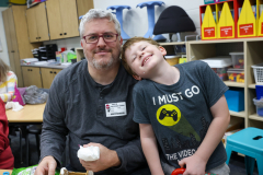 Man and child in a classroom setting, smiling at the camera.