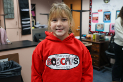 Girl in red hoodie standing in front of desk.