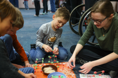 A woman and three children are engaged in a craft activity involving building structures with toothpicks and marshmallows.