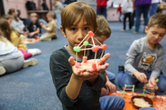 Young boy holding a gingerbread house in a classroom setting.