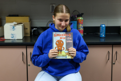 Girl holding up a book in front of her face.