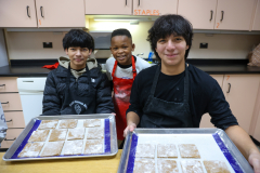 Three people in a kitchen, preparing gingerbread cookies for Christmas.