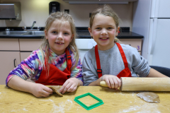 Two young girls in a kitchen, one holding a rolling pin, both smiling at the camera.