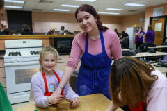 Woman in blue apron standing behind children at table with flour.