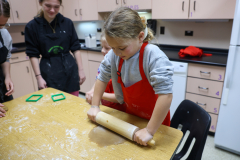 Young girl in apron making gingerbread cookies at kitchen counter.
