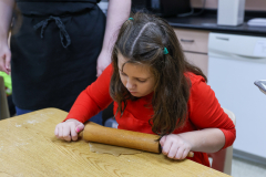 Little girl in red shirt rolling out dough on countertop.