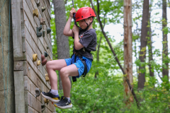 Person in red helmet climbing rock wall at camp.