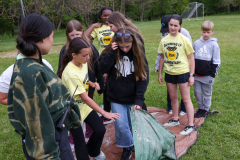 Group of people in a field, some standing around a tent, others looking at something on the ground.