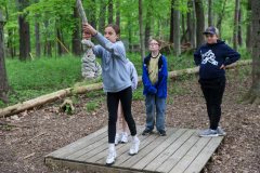 Three people standing on a wooden platform in a forested area, looking at something off-camera.