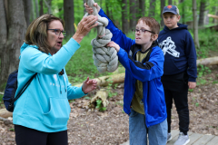 Woman in blue jacket teaching young boy how to tie a rope into a knot.