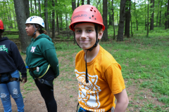 A young boy wearing a red helmet stands in front of a group of people at camp eberhart.