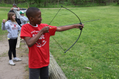 Young boy in red shirt holding a bow and arrow, preparing to shoot.