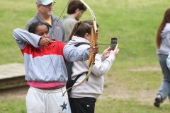 Two people aiming bows at a target in an outdoor setting.