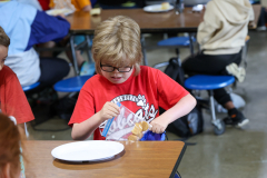 A young boy in a wheelchair eating food at a table.