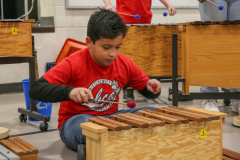 Young boy playing a wooden xylophone in a school setting.