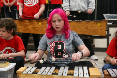 Young girl playing a drum set in front of an audience during a concert.