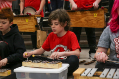 Three children playing musical instruments in a group setting.