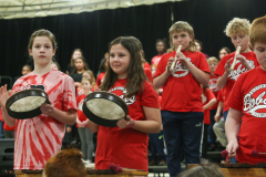 Three children playing drums in a school concert.