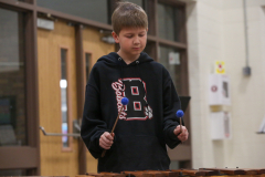 Young boy playing a drum set in a school gymnasium.