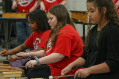 Three children playing musical instruments in a school event.