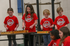 Three children playing musical instruments in a school setting.