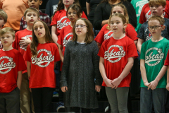 Children in red shirts standing on stage at a school concert.