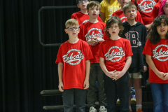 Young students in red shirts standing on stage at a school concert.