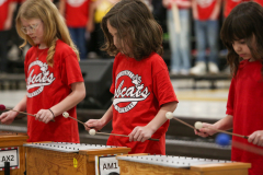 Three children playing musical instruments in a group setting.