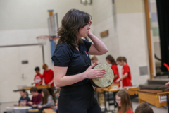 Woman in black shirt holding a tambourine during a school concert.