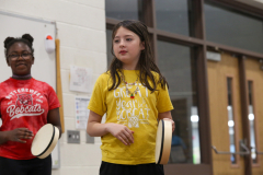 Girl in yellow shirt holding a drumstick, smiling at camera.