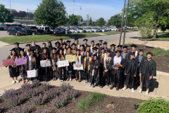 Graduates posing in front of a building, holding signs and celebrating their achievement.