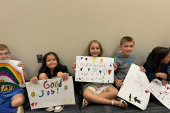 Children sitting on the floor, holding signs and posters.