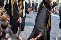 Graduates in caps and gowns walking across a stage.