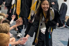 Graduating students walking in procession, smiling as they receive high fives from audience.