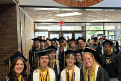 A group of graduating students posing in front of a school sign, proudly displaying their academic achievements and