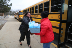 Bus driver handing gift to passenger at bus stop.