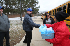 Two people handing over a gift bag in front of a school bus.