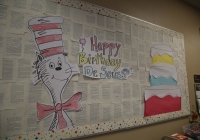 Happy birthday dr. seuss day board with cat in hat next to cake.