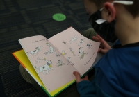Child reading a book in front of a blue wall.