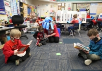 Three children sitting on floor reading books in a classroom during Dr. Seuss Day celebration.