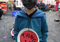 Young boy in a classroom setting wearing a face mask and a Dr. Seuss themed shirt.