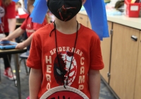 Boy wearing a mask and costume standing in front of a classroom.