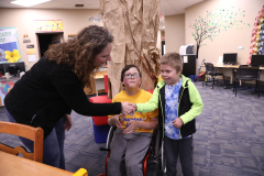 Woman in wheelchair shaking hands with two young boys in a library setting.