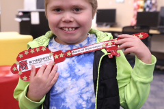 Young boy proudly holding a red dog bone shaped key chain in front of his face.