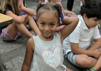 Little girl in a classroom setting, smiling at the camera on her first day of kindergarten.
